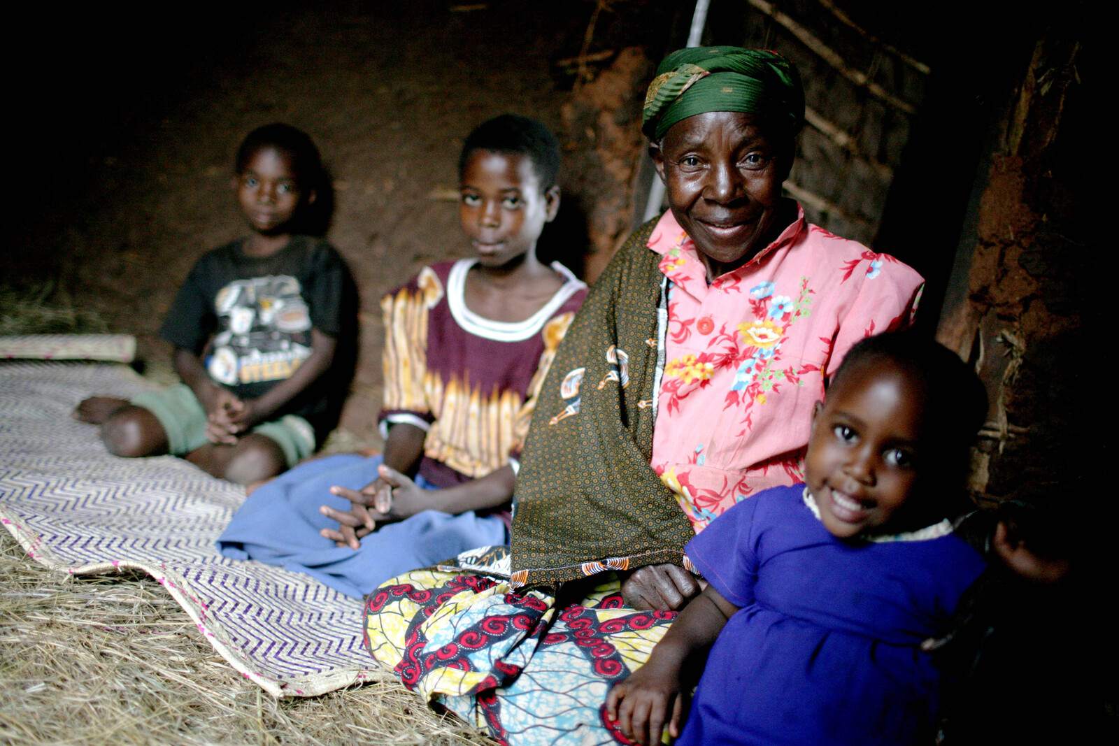 Together with small children, an old woman is sitting on the ground. 