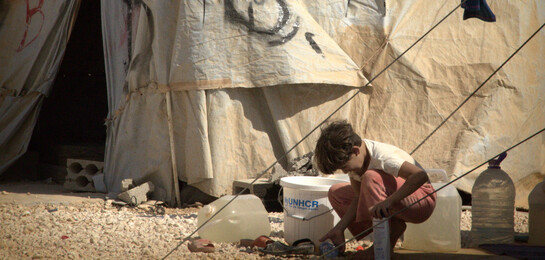 Ein syrisches Kind kniet vor einer Notunterkunft.