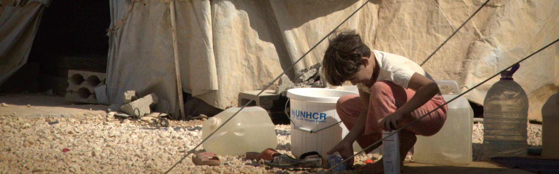Ein syrisches Kind kniet vor einer Notunterkunft.