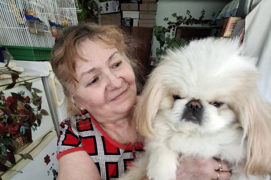 Eine ältere Frau hält einen kleinen weißen Hund in ihren Händen und lächelt ihn an