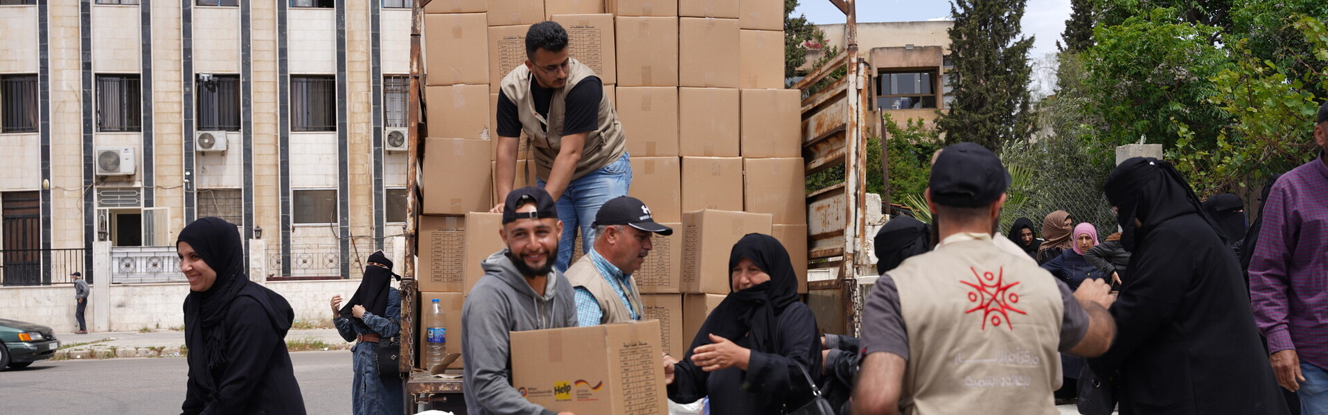 Helfer von Help reichen verschiedenen Menschen Hilfsgüter aus einem Lastwagen