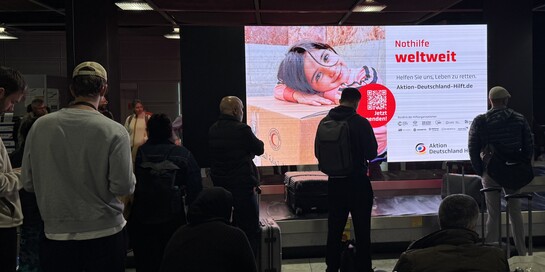 Außenwerbung von Aktion Deutschland Hilft an einem Gepäckband am Flughafen