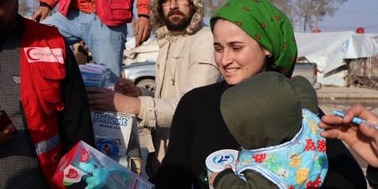 Eine syrische Frau erhält von einem Helfer Babynahrung und Spielzeug für ihr Kind