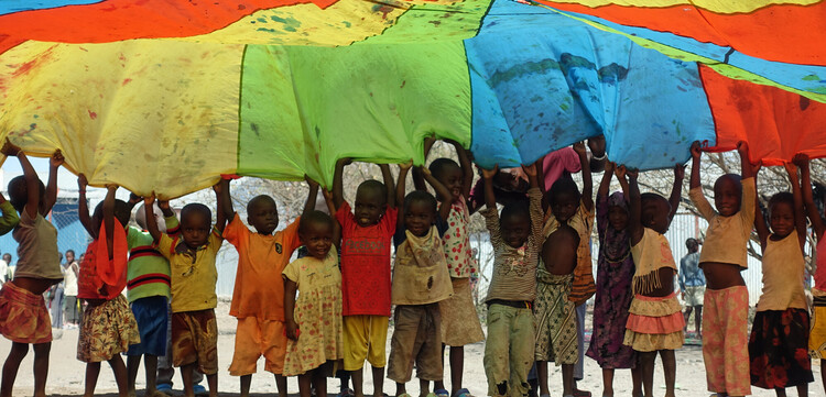 Kinder im Geflüchtetencamp Kakuma spielen mit einem bunten Schwungtuch Kinder im Geflüchtetencamp Kakuma spielen mit einem bunten Schwungtuch