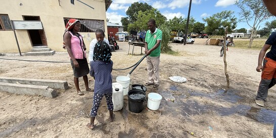 Nach dem Zyklon in Mosambik füllt ein Helfer sauberes Wasser in einen Eimer. Ein paar weitere Erwachsene und Kinder stehen daneben