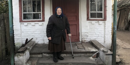 Eine Seniorin steht vor ihrem kleinen Haus in der Ukraine