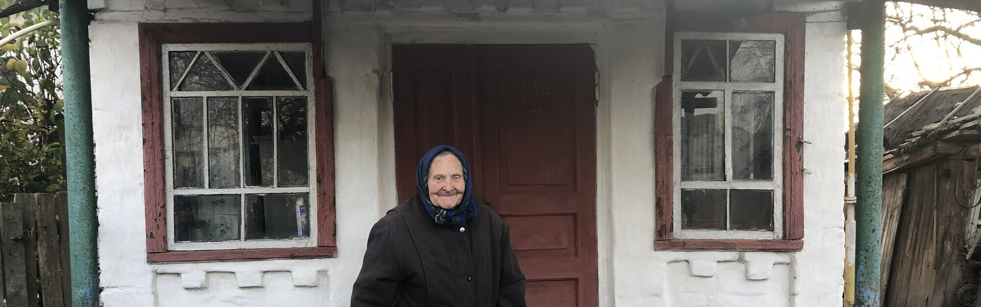 Eine Seniorin steht vor ihrem kleinen Haus in der Ukraine