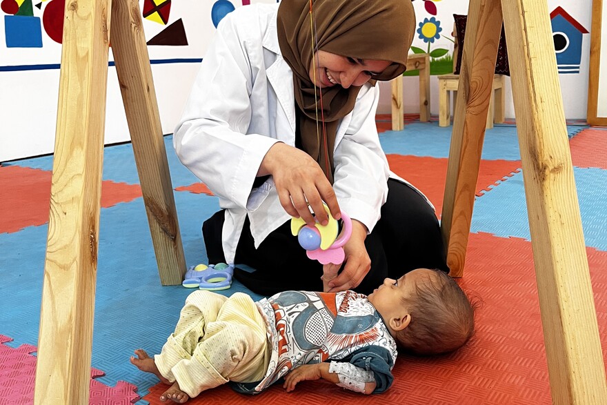 Eine Helferin macht mit einem Baby in Afghanistan eine spielerische Bewegungstherapie