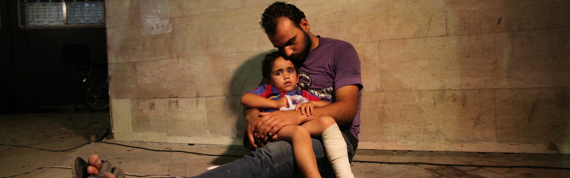 Mann sitzt mit Kind auf dem Boden.Beide sind auf der Flucht in Syrien.