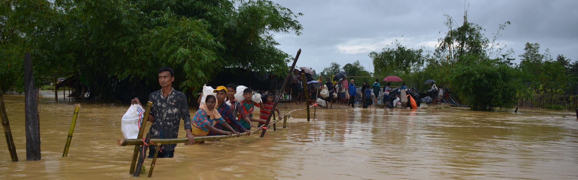 Eine Menschenkette in Bangladesch hangelt sich an einer Bambusstange durch die Fluten (Archivbild)