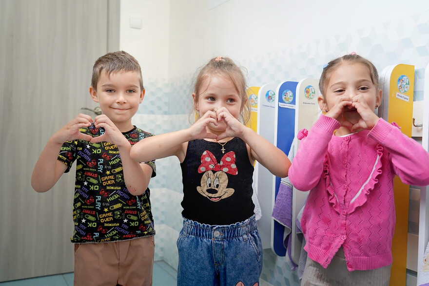 Drei Kinder aus der Ukraine zeigen ein Herzsymbol mit ihren Händen und lächeln
