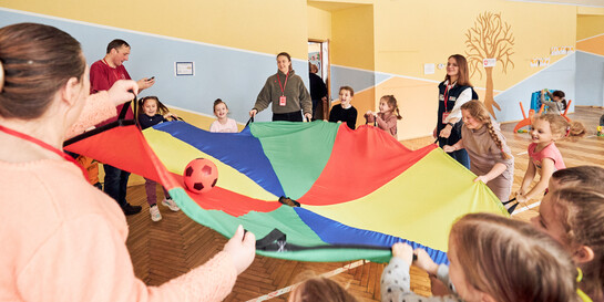 Kinder balancieren einen Ball in einem bunten Fallschirm-Schwungtuch