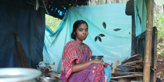 Eine Frau in Indien sitzt auf einem Holzhocker in einer mit Tüchern bedeckten Unterkunft (Archivbild)