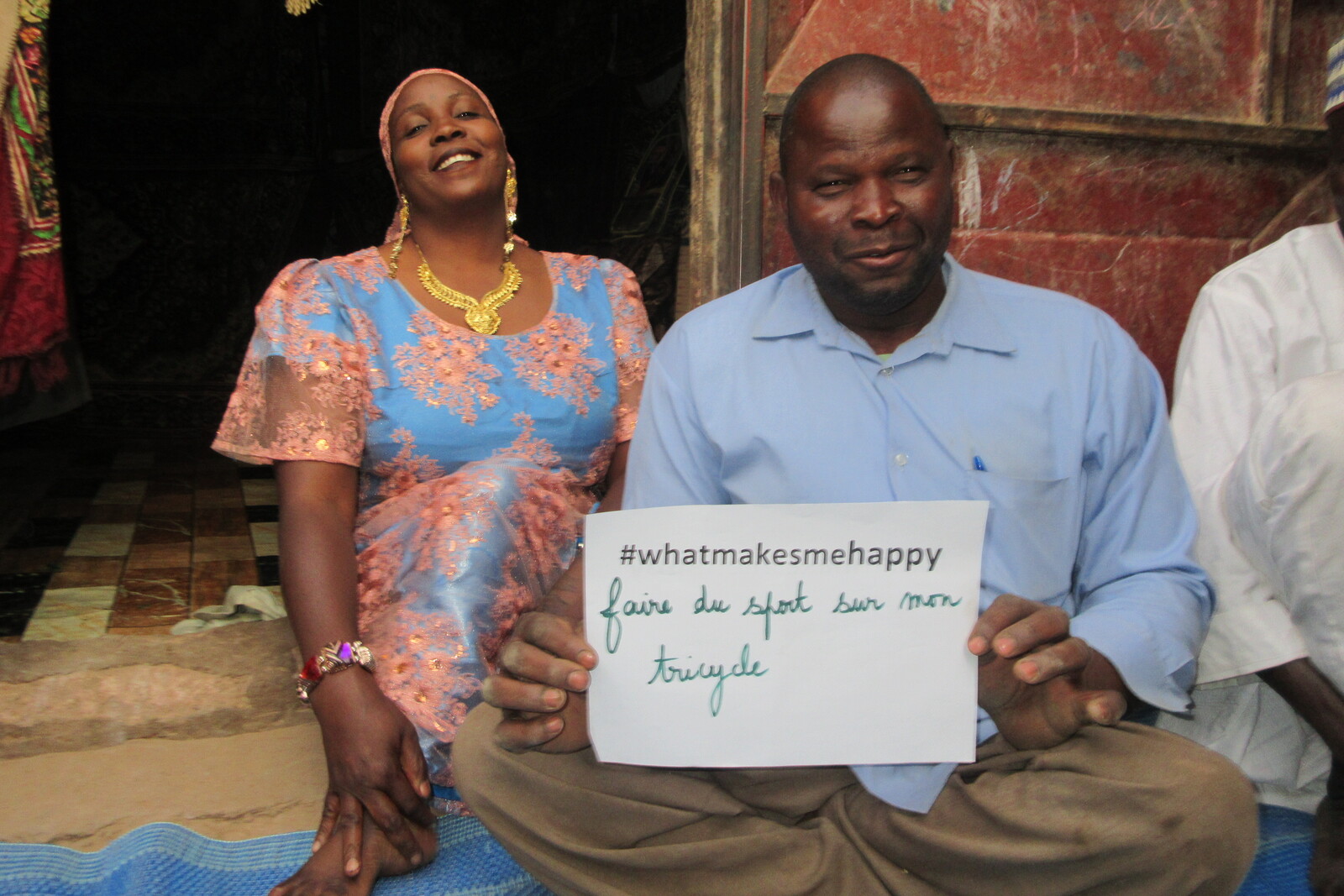 Mann und Frau sitzen auf dem Boden und halten ein Schild hoch mit der Aufschrift "#whatmakesmehappy"