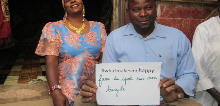 Mann und Frau sitzen auf dem Boden und halten ein Schild hoch mit der Aufschrift "#whatmakesmehappy"