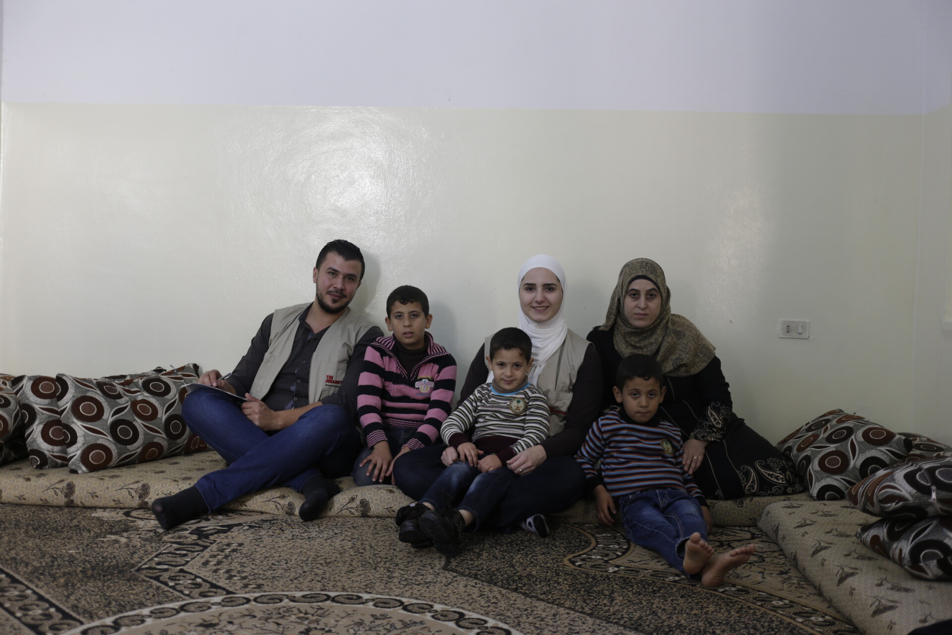 Flüchtlingsfamilie sitzt mit Kindern vor einer Wand Flüchtlingsfamilie sitzt mit Kindern vor einer Wand