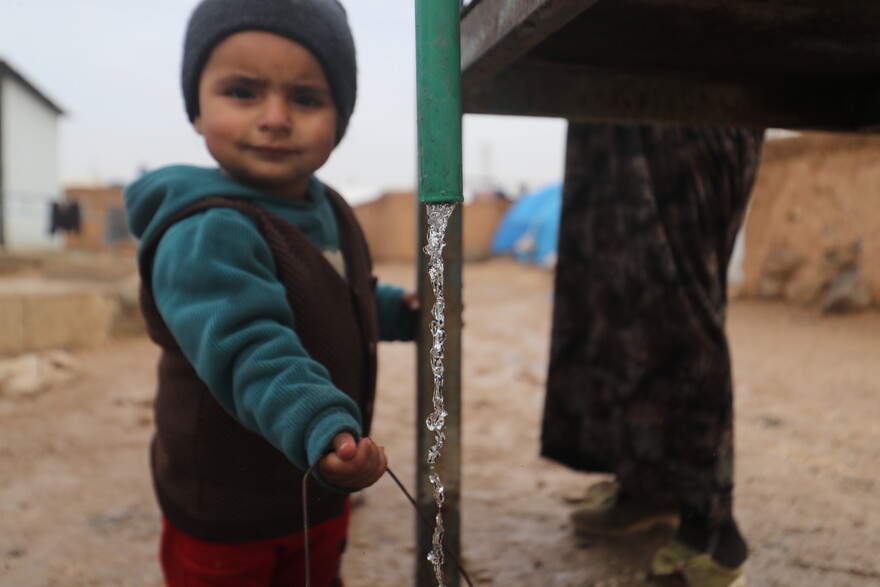 Ein kleiner Junge steht neben einem Wassertank, aus dem klares Wasser fließt