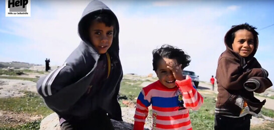 Help unterstützt Flüchtlinge in Jordanien. Drei Kinder stehen auf offenem Feld in Jordanien.