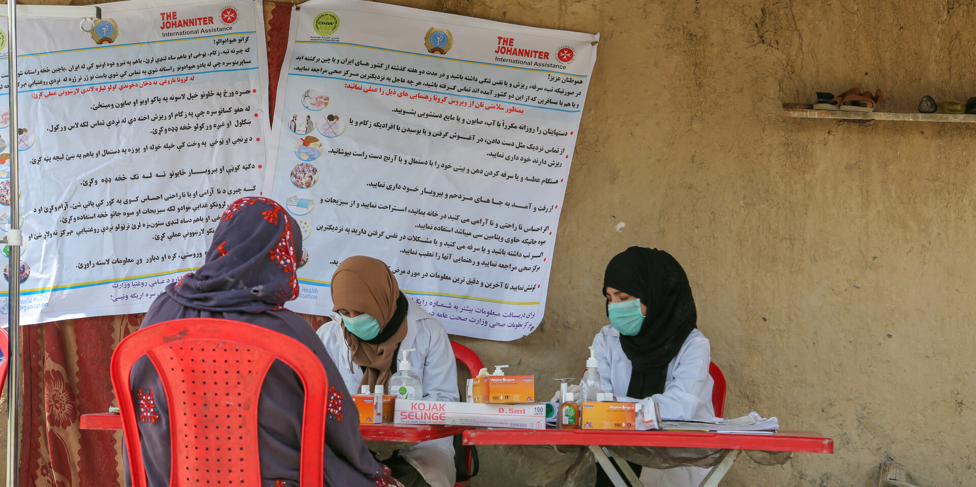 Drei afghanische Frauen sitzen mit Mundschutz an einer Hygienestation der Johanniter Drei afghanische Frauen sitzen mit Mundschutz an einer Hygienestation der Johanniter