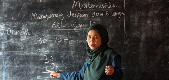 In Indonesien wird das Bildungssystem ausgebaut. Eine Lehrerin steht vor einer Tafel und unterrichtet Lesen und Schreiben.