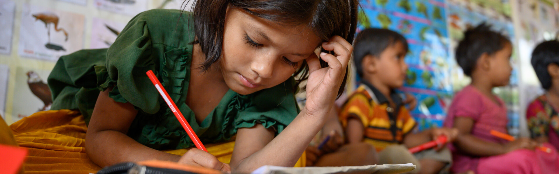 Ein Mädchen in Bangladesch schreibt mit einem Bleistift in ein Schulbuch Ein Mädchen in Bangladesch schreibt mit einem Bleistift in ein Schulbuch
