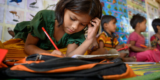 Ein Mädchen in Bangladesch schreibt mit einem Bleistift in ein Schulbuch