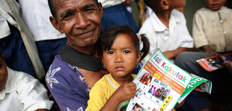 Auf dem Schoß eines Mannes in Laos sitzt ein Mädchen mit Kinderzeitschrift in den Händen Auf dem Schoß eines Mannes in Laos sitzt ein Mädchen mit Kinderzeitschrift in den Händen