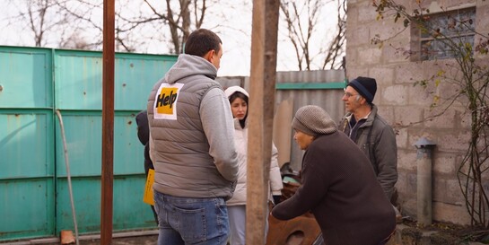 Fünf Personen stehen draußen, neben einem Haus in der Ukraine. Einer der Männer trägt die Aufschrift Help auf dem Rücken