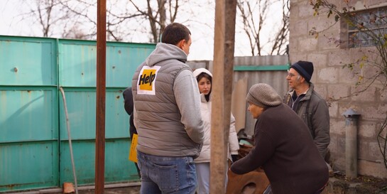 Fünf Personen stehen in einem Innenhof zwischen zwei Häusern in der Ukraine. Einer der Männer trägt die Aufschrift Help auf dem Rücken