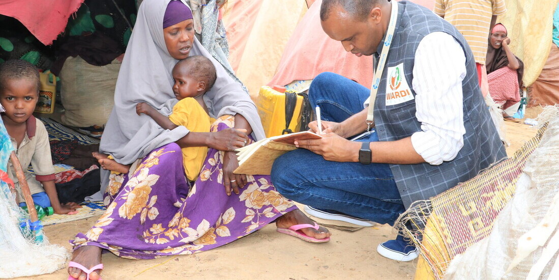 Ein Helfer in Somalia spricht mit einer Frau, die mit ihren Kindern in einer Notbehausung wohnt
