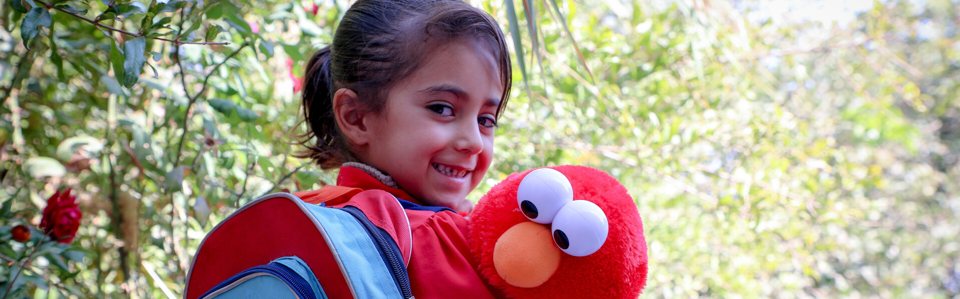 Ein Mädchen in Afghanistan mit rotem World-Vision-Rucksack und Elmo-Stofftier 