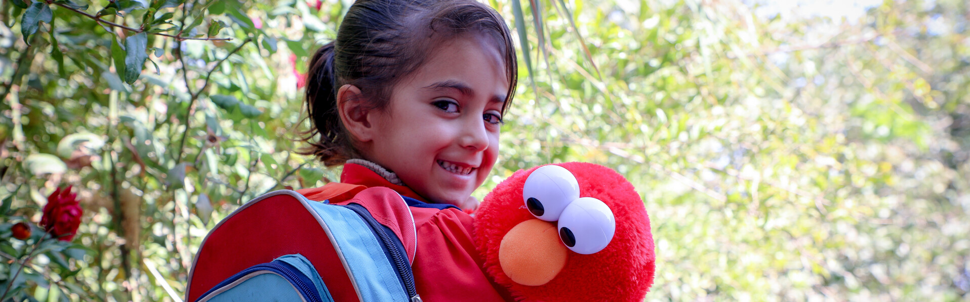 Ein Mädchen in Afghanistan mit rotem World-Vision-Rucksack und Elmo-Stofftier 