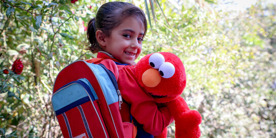Ein Mädchen in Afghanistan mit rotem World-Vision-Rucksack und Elmo-Stofftier 