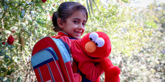 Ein Mädchen in Afghanistan mit rotem World-Vision-Rucksack und Elmo-Stofftier 