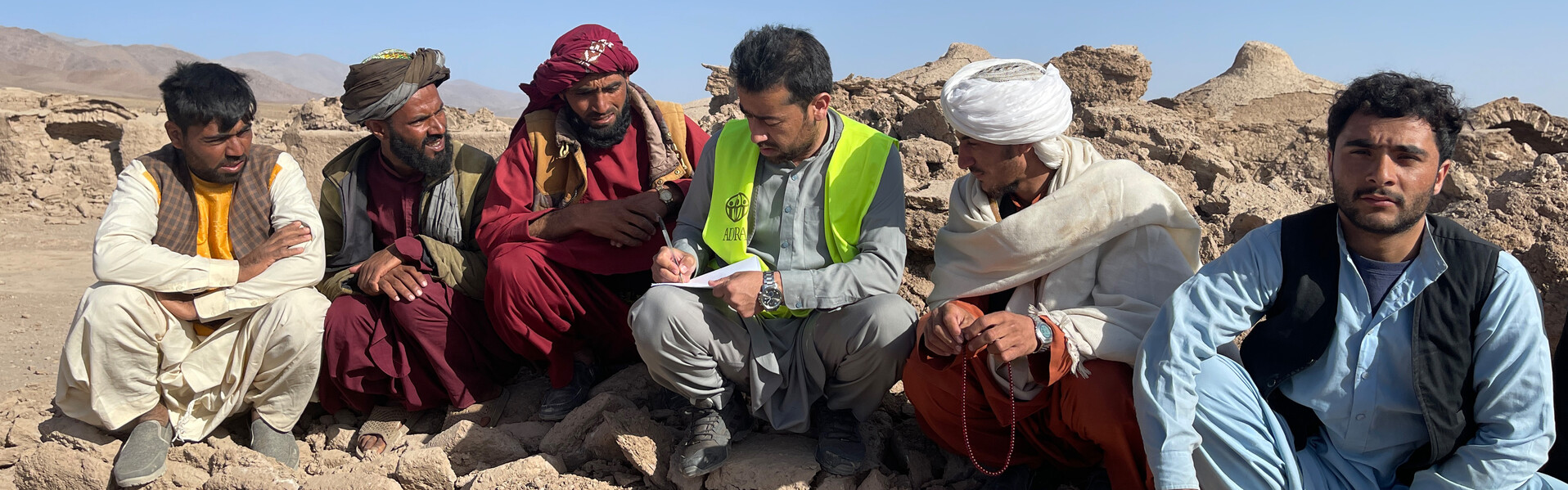 Eine Gruppe von Männern sitzt zwischen den Trümmern eingestürzter Gebäude nach einem Erdbeben und organisiert Hilfsmaßnahmen (Symbolbild)