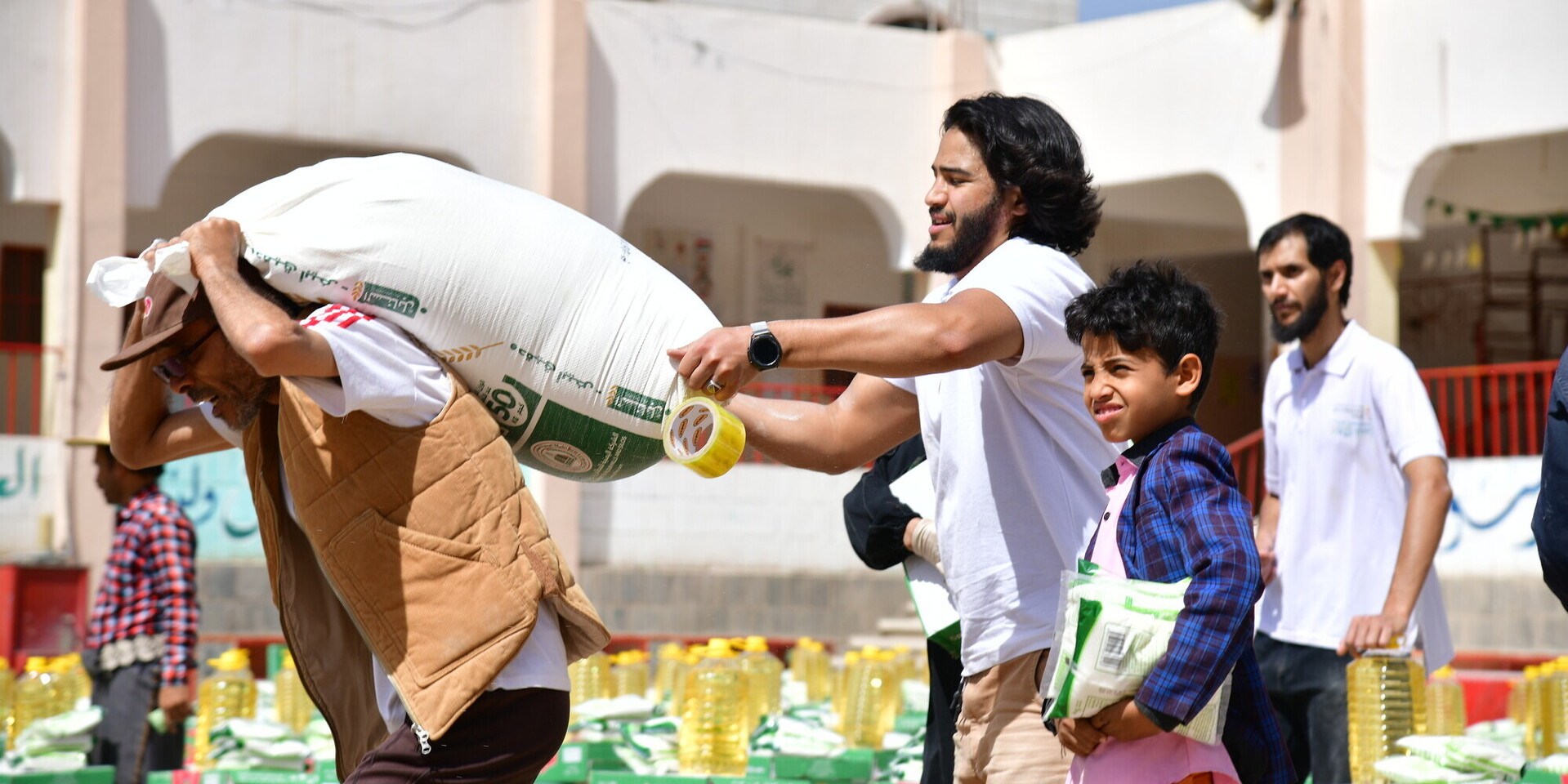 Drei Männer und ein Kind bei der Verteilung von Hilfsgütern im Jemen