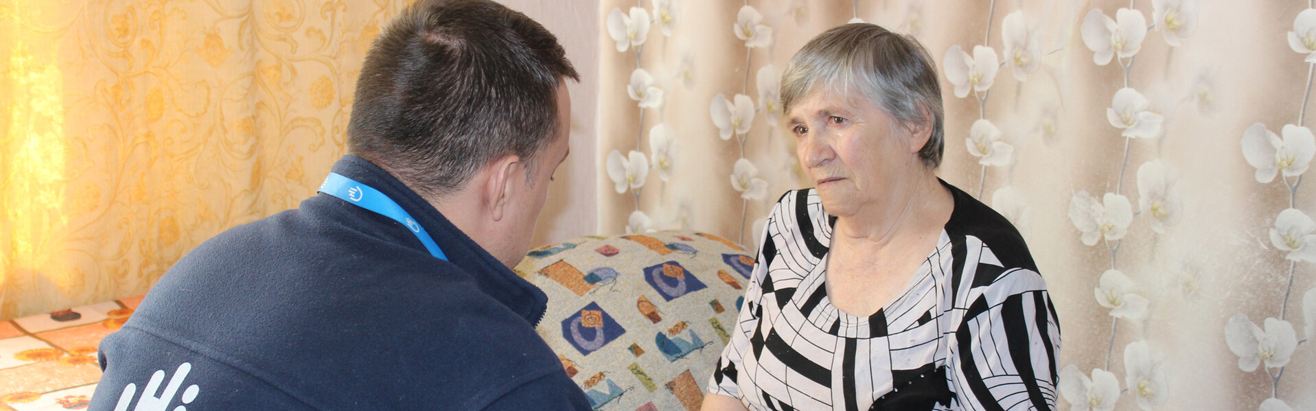 Lidiya spricht mit einem Helfer von Handicap International Eine ältere ukrainische Frau sitzt auf einem Bett, vor ihr ein humanitärer Helfer, der mir ihr spricht