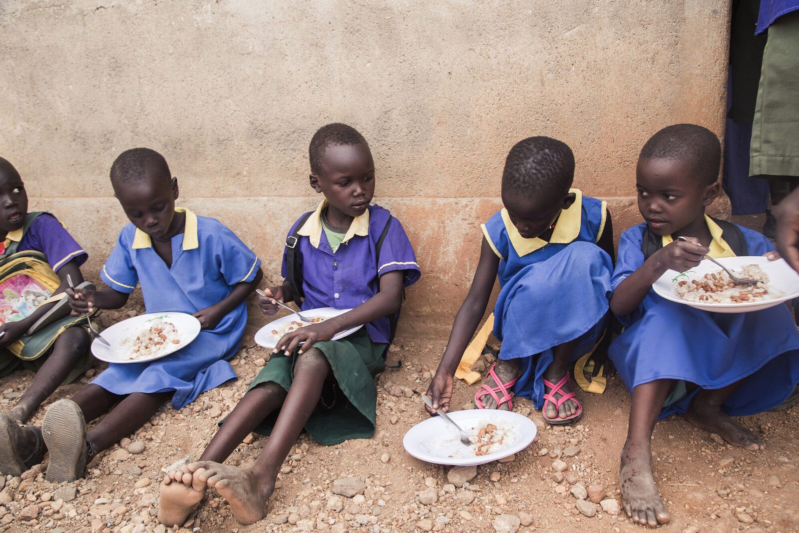 Eine Gruppe von Schulkindern im Südsudan isst auf dem Fußboden Reis mit Bohnen 