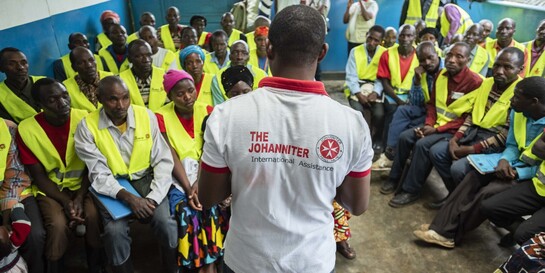 Ein Helfer der Johanniter spricht vor einer Gruppe von Menschen im Kongo