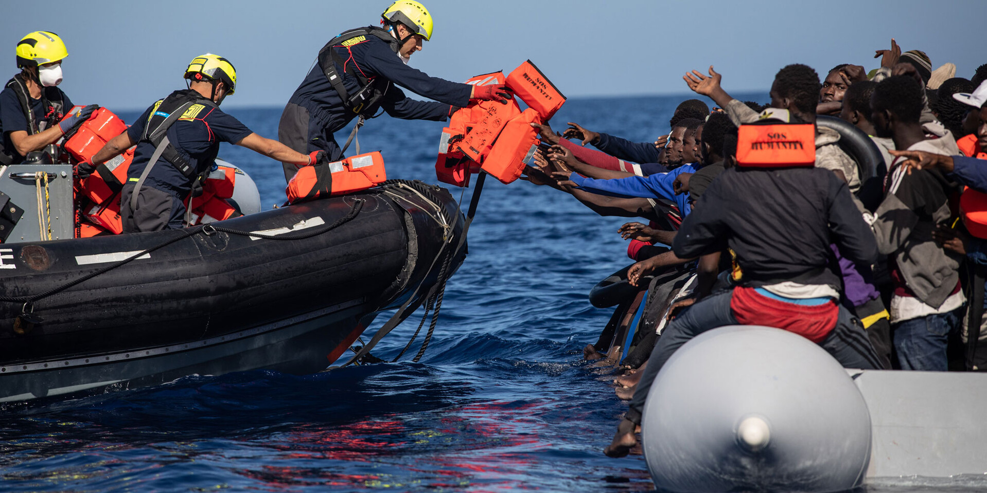 Ein Helfer von SOS Humanity reicht Menschen auf einem Boot Rettungswesten an