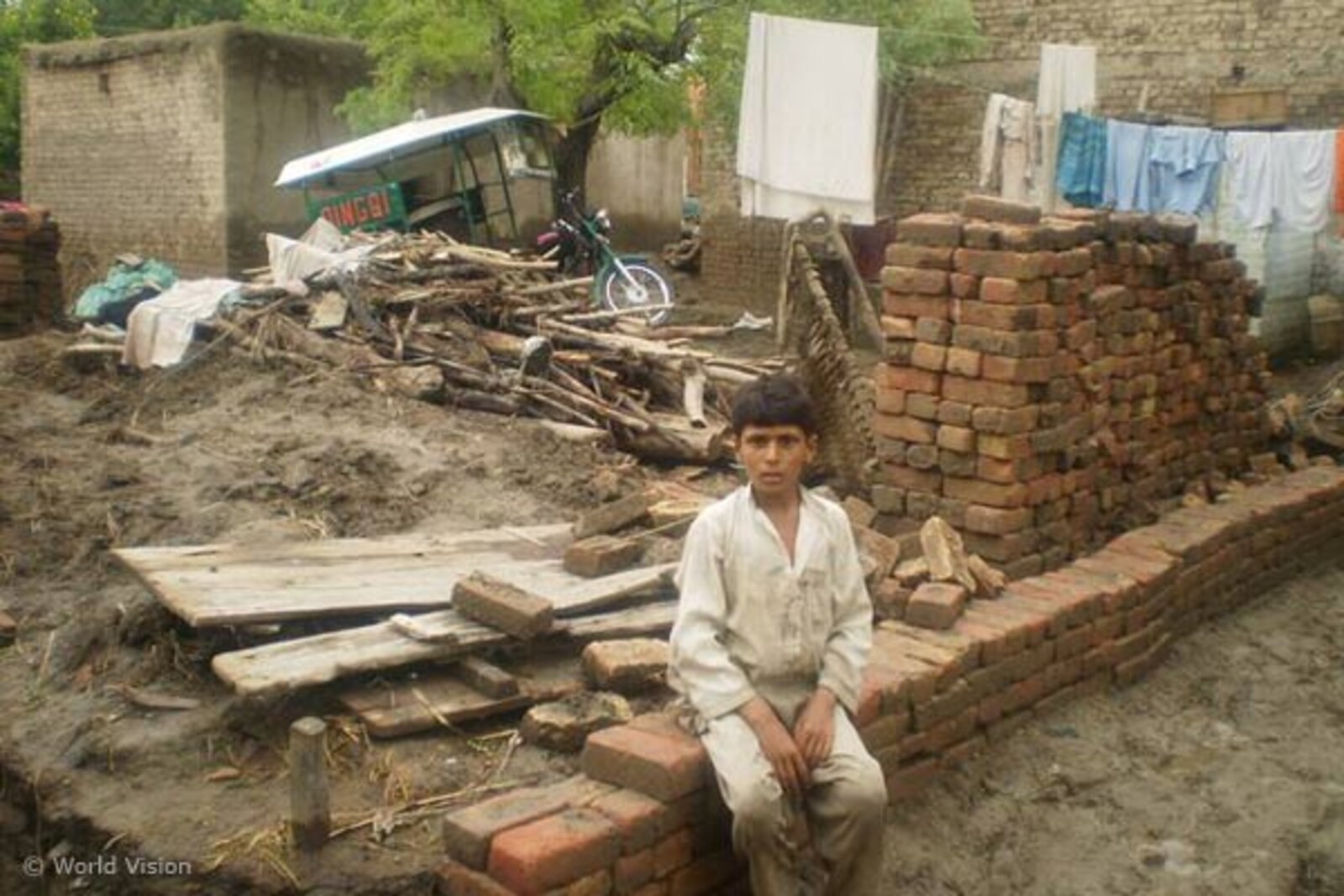 junge-auf-mauer Flut Pakistan: Junge baut ein Haus aus Ziegeln
