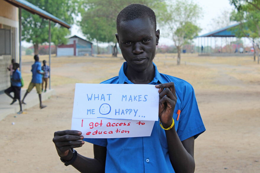 Ein Mann hält ein Schild hoch mit der Aufschrift "What Makes You Happy - I got access to education"