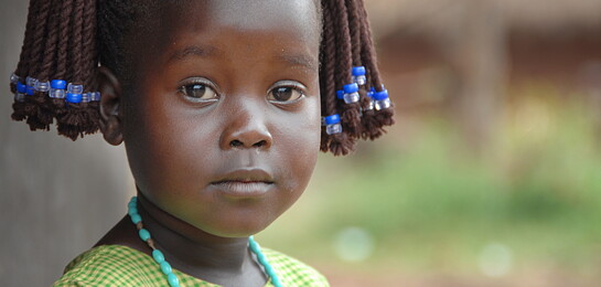 In Uganda steht ein Mädchen vor einer Hütte.