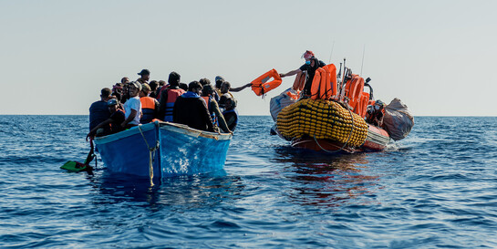 Ein Rettungsschiff verteilt auf einem überfüllten Boot Schwimmwesten an Geflüchtete 