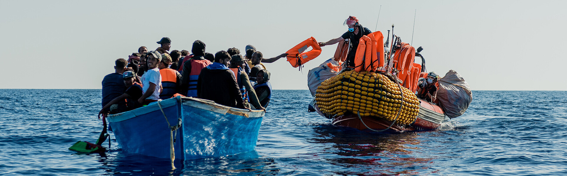 Ein Rettungsschiff verteilt auf einem überfüllten Boot Schwimmwesten an Geflüchtete 