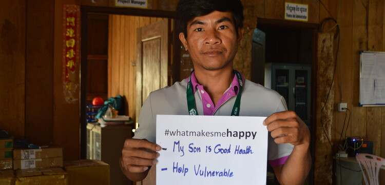 Ein Mann hält in Kambodscha ein Zettel hoch mit der Aufschrift "What Makes Me Happy - My son is good health / help vulnerable"
