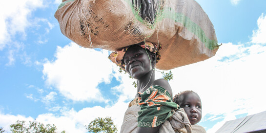 Eine Frau in Uganda trägt ihr Baby in einem Tuch auf dem Rücken