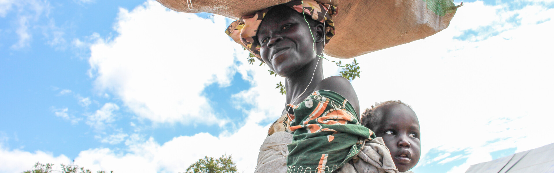 Eine Frau in Uganda trägt ihr Baby in einem Tuch auf dem Rücken