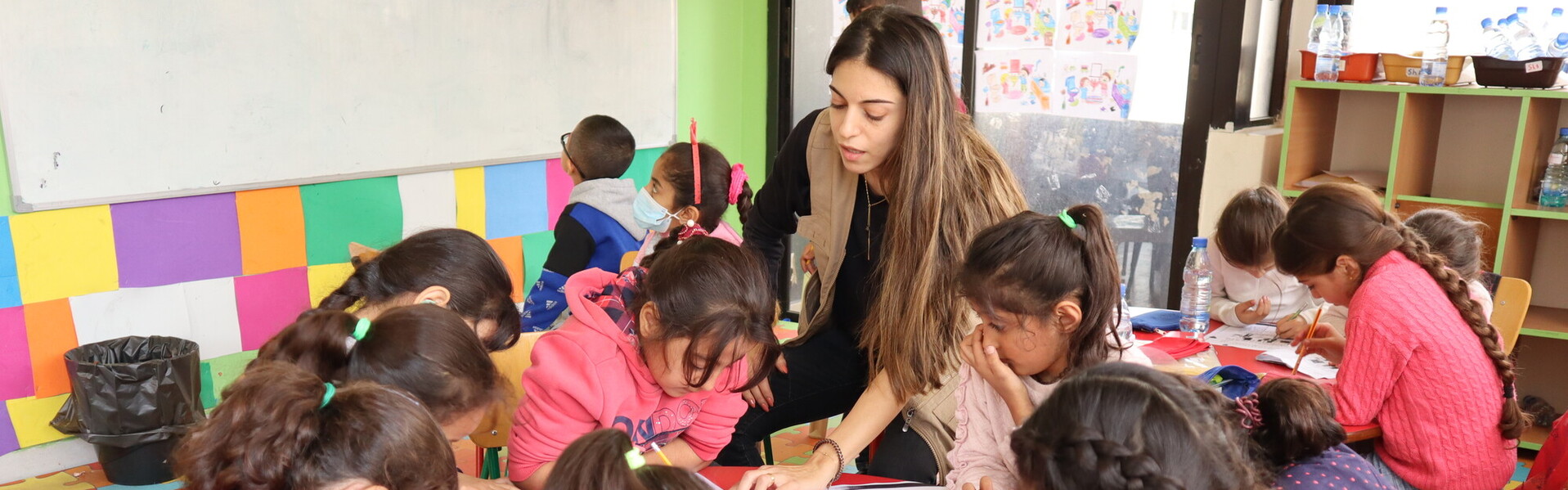 Eine Helferin steht in einer Schule im Libanon umgeben von einer Gruppe von Kindern, die gemeinsam malen. Eine Helferin steht in einer Schule im Libanon umgeben von einer Gruppe von Kindern, die gemeinsam malen.