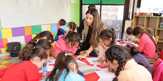 Eine Helferin steht in einer Schule im Libanon umgeben von einer Gruppe von Kindern, die gemeinsam malen.